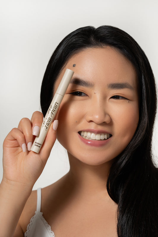 Smiling woman holding Light Heart Brow Growth Serum beside her face, showcasing a brow-enhancing treatment for fuller, healthier-looking eyebrows.